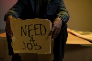 A man holding a cardboard sign reading 'Need a Job', symbolizing unemployment and hardship.