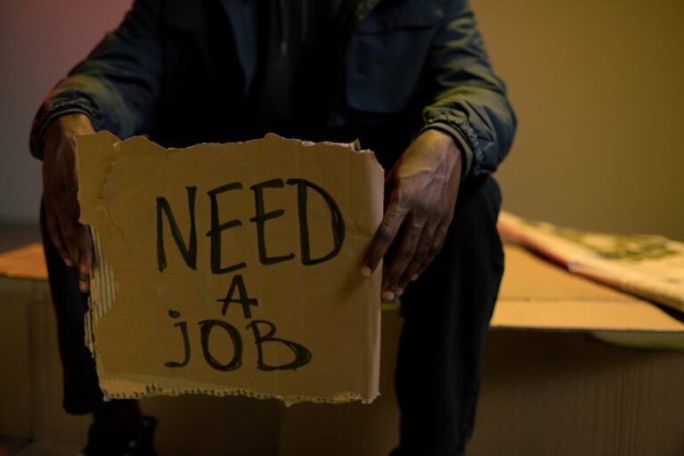 A man holding a cardboard sign reading 'Need a Job', symbolizing unemployment and hardship.
