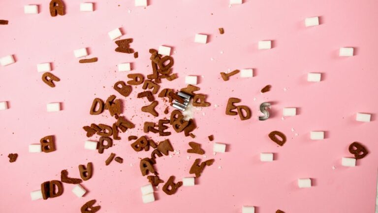Scattered letters and sugar cubes on a pink background creating an artistic concept.