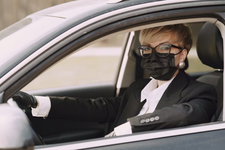 A woman wearing a mask and gloves drives a car, emphasizing safety during the pandemic.