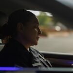 Policewoman in uniform writing notes inside a patrol car during the day.