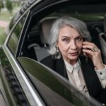 Confident senior businesswoman communicating on smartphone while seated in a luxurious car interior.