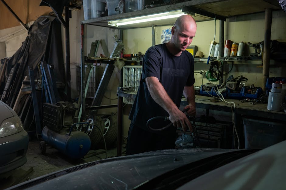 Bald mechanic focused on repairing a car engine in a garage setting.