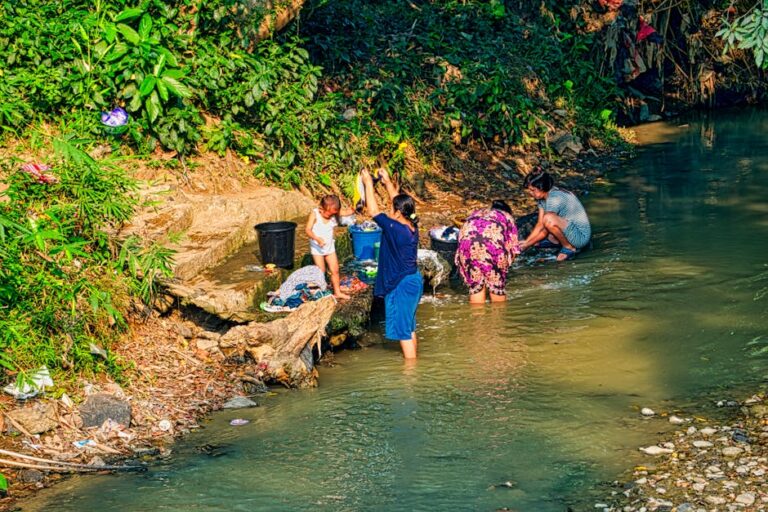 People washing clothes in a scenic river setting in West Java, Indonesia.