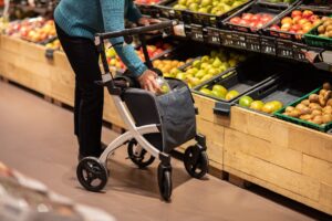 Senior woman with mobility aid choosing fresh fruits in a supermarket aisle.