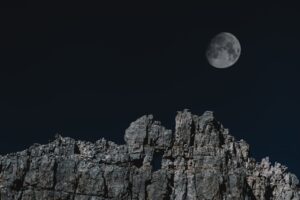 Scenic night view of a full moon rising above rocky cliffs against a dark sky.