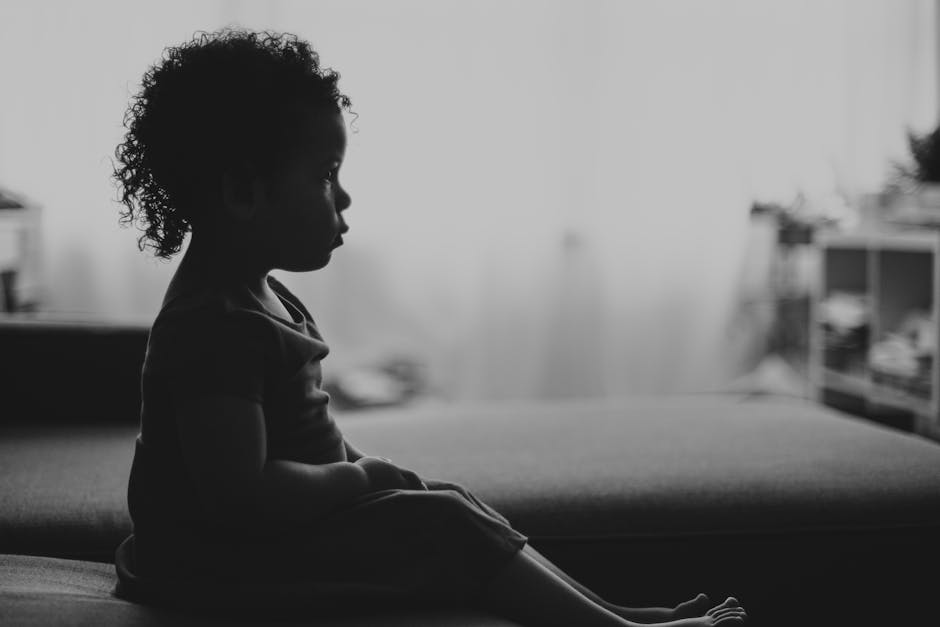 Black and white silhouette of a toddler sitting on a couch in a softly lit room.