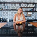 Woman in kitchen smiling over healthy breakfast plate, showcasing modern interior design