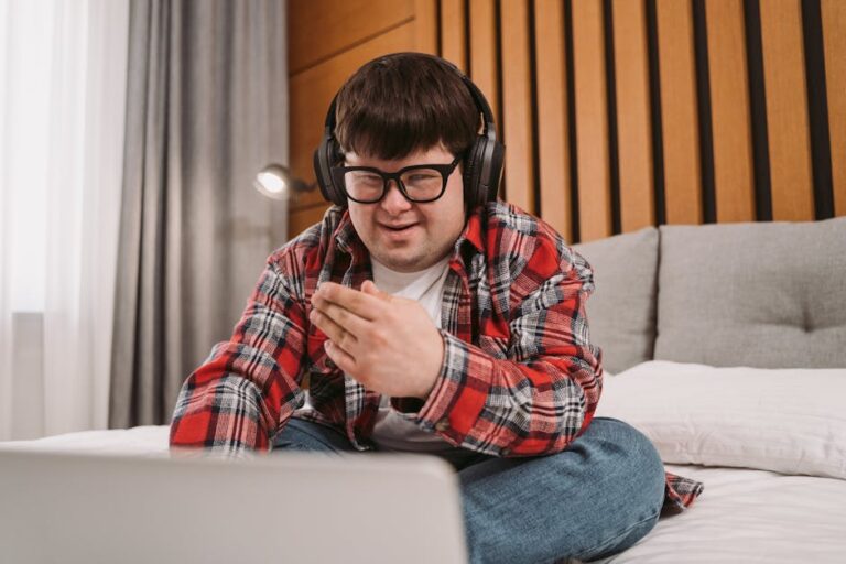 Smiling young man with Down syndrome using laptop and headphones indoors.