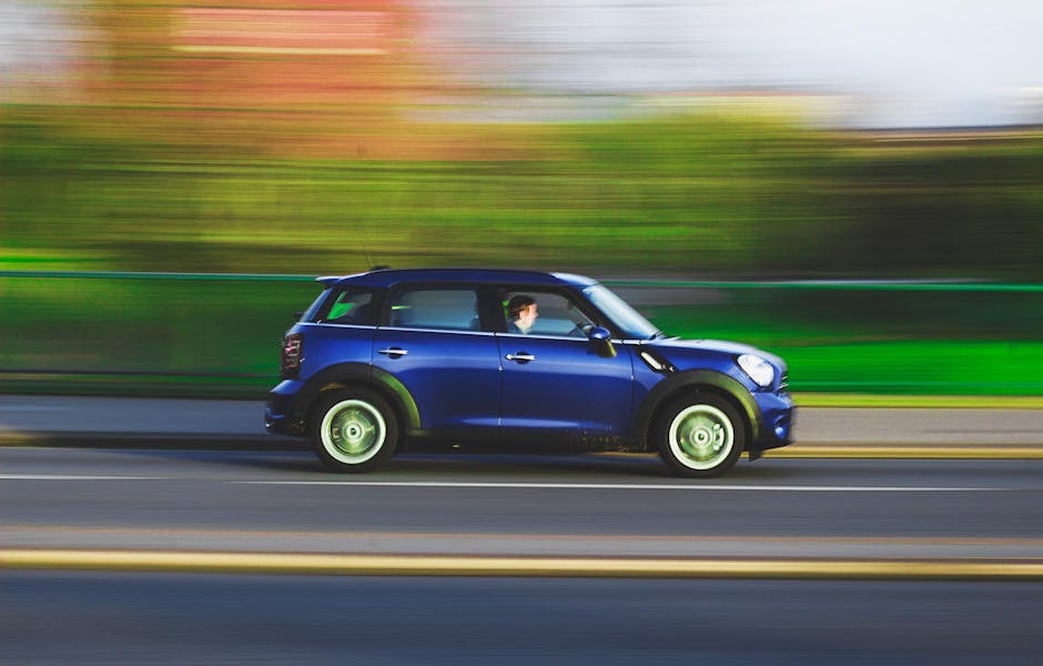 A blue car swiftly drives on a road with a blurred background, capturing speed and movement.