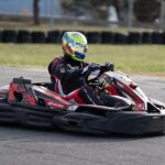 A go-kart driver in full gear racing on an outdoor track during the day.