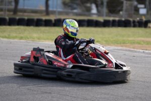 A go-kart driver in full gear racing on an outdoor track during the day.