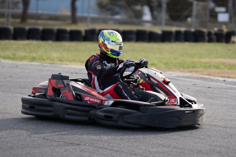 A go-kart driver in full gear racing on an outdoor track during the day.
