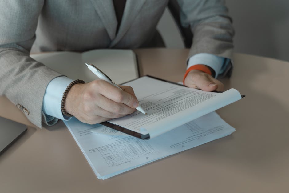 Close-up of business person signing documents at a desk with a pen.
