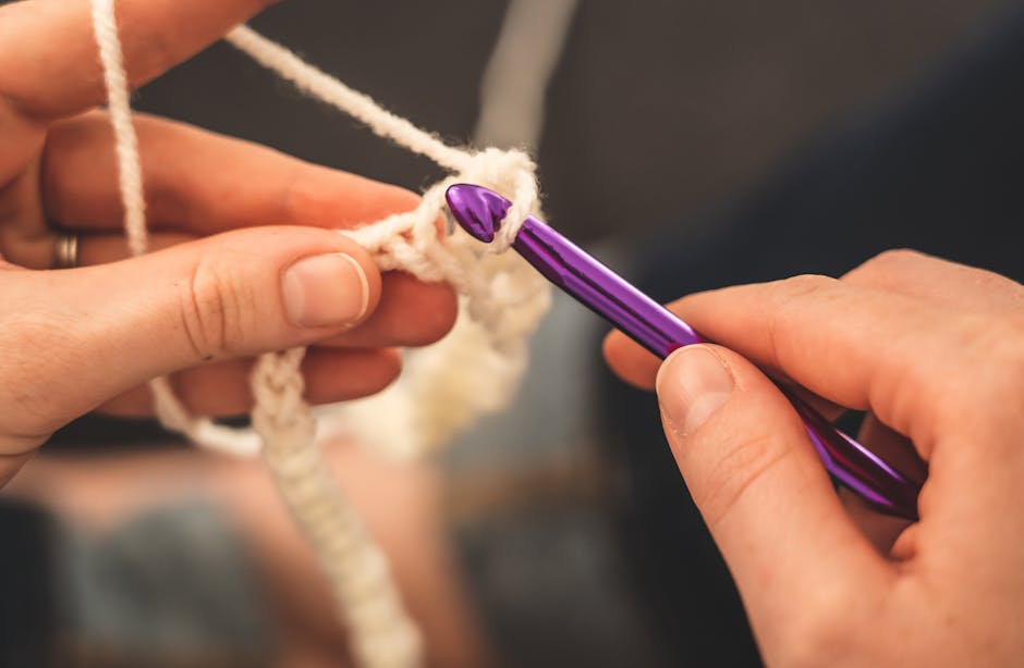 Hands skillfully crocheting with a purple hook and cream yarn, highlighting craftsmanship.