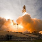 Dramatic view of a space shuttle launching, surrounded by smoke and fire.