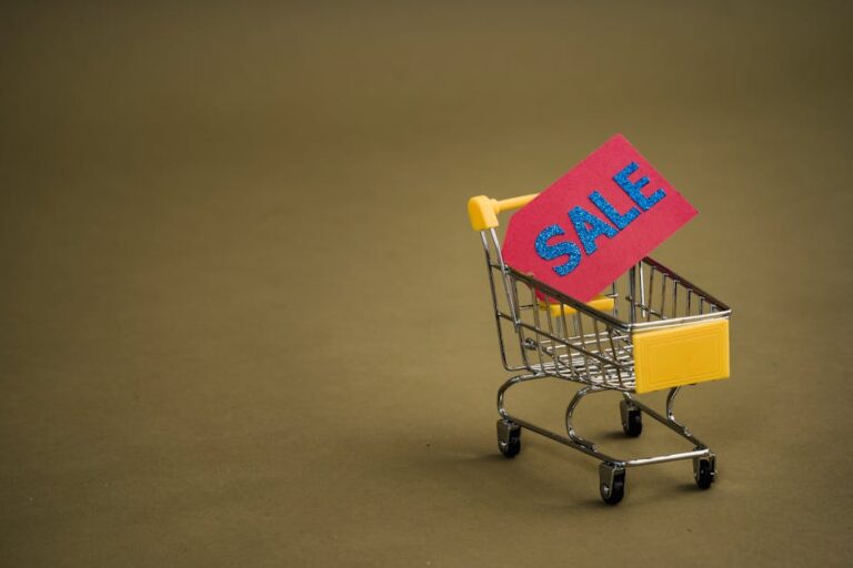 A miniature shopping cart with a bright red 'SALE' tag on a neutral brown background.