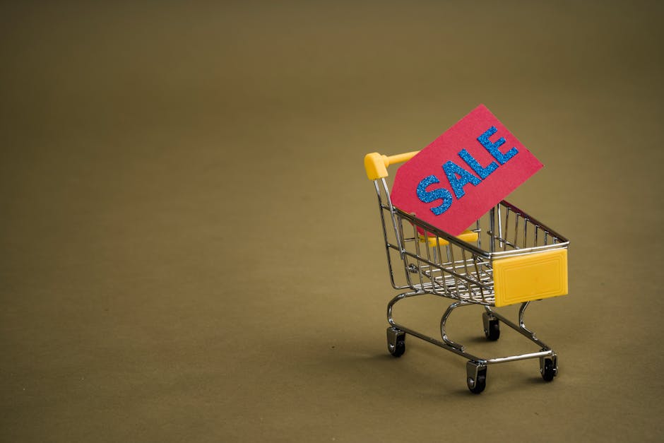 A miniature shopping cart with a bright red 'SALE' tag on a neutral brown background.