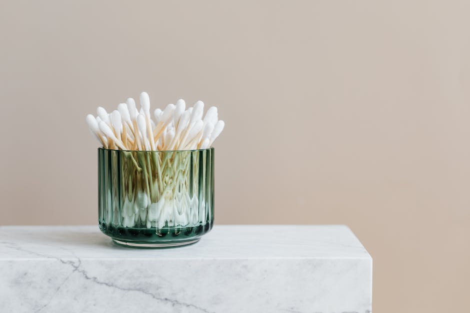 Aesthetic arrangement of cotton swabs in a green glass jar on a marble surface.