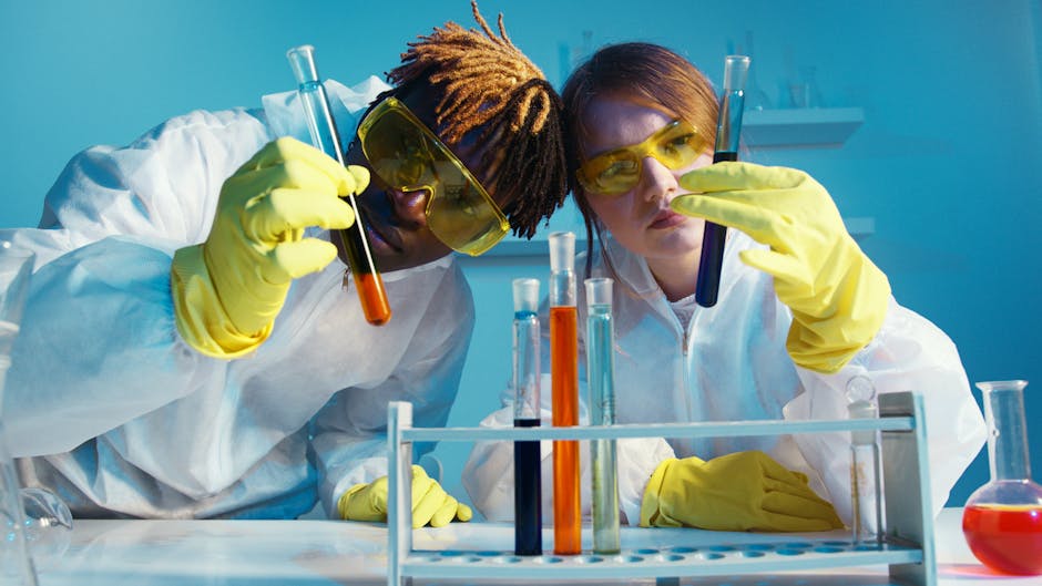 Two scientists in protective gear analyzing test tubes in a laboratory setting.