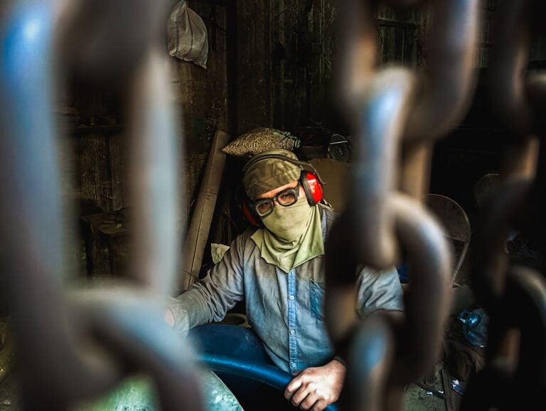 A masked industrial worker seen through hanging chains, focused on safety in a workshop environment.