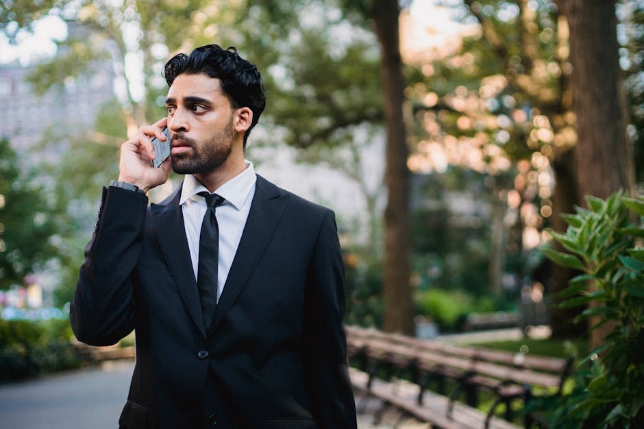 A well-dressed man in a suit makes a phone call in an urban park setting.