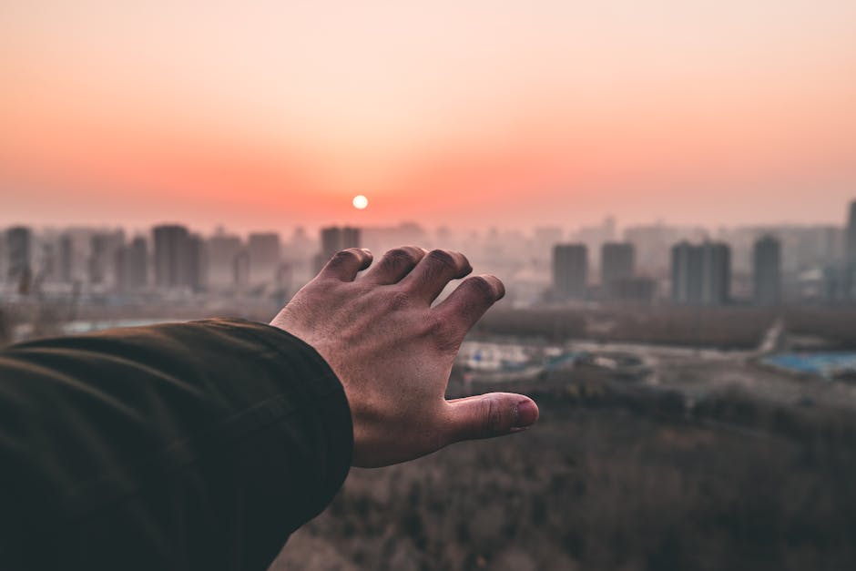 A hand reaching out towards a sunset over a city's skyline, evoking themes of aspiration and connection.