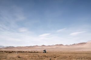 A lone vehicle navigates a remote desert landscape under a vast, clear blue sky.