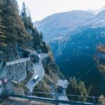 A breathtaking high angle view of a mountain road with a tunnel and a van driving through a pine tree forest.