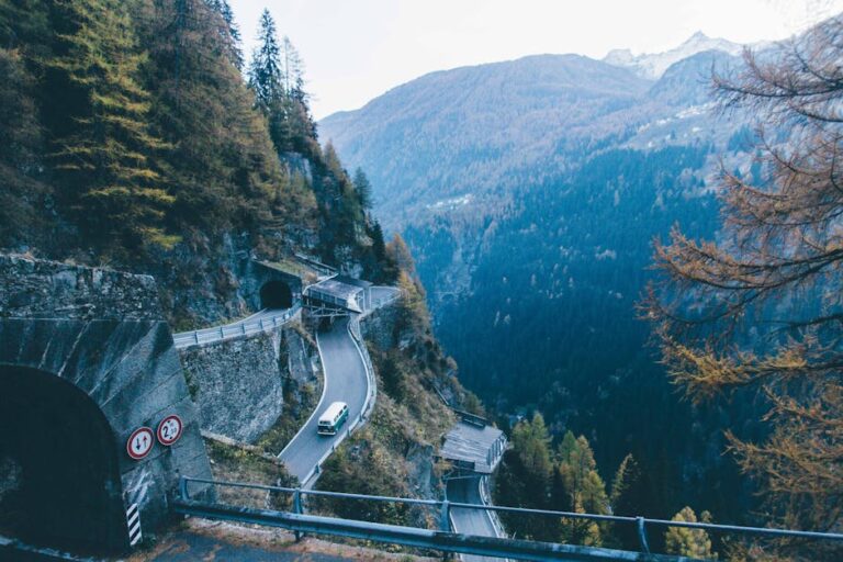A breathtaking high angle view of a mountain road with a tunnel and a van driving through a pine tree forest.