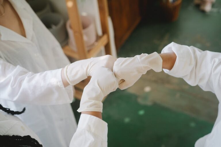 Close-up of healthcare professionals in white lab coats and gloves fist bumping in a laboratory environment.