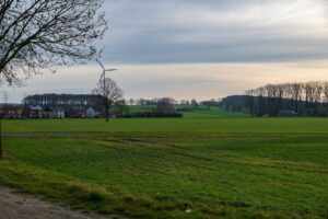 Peaceful countryside scene featuring a wind turbine amid vast green fields under a calm sky.