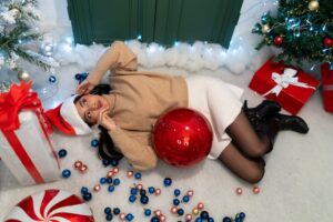 Woman in Santa hat lying on floor with Christmas gifts and decorations.