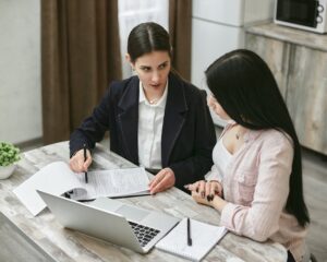 Two businesswomen engaged in a contract discussion at an office table.