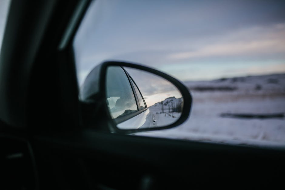 View of Iceland's winter landscape through a car mirror, capturing reflection, snow, and travel.